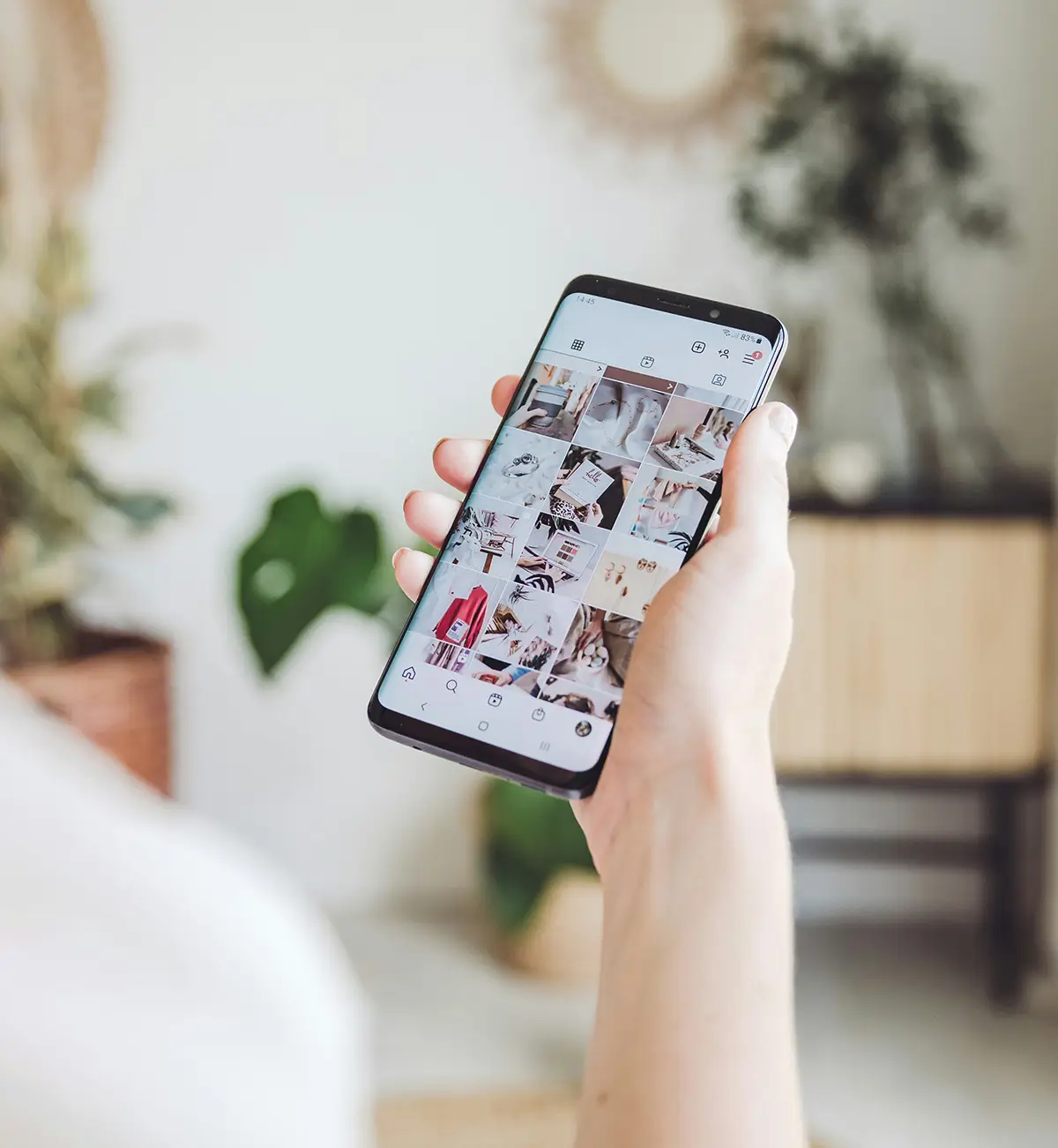 a hand holding a cellphone, with a social media feed on screen
